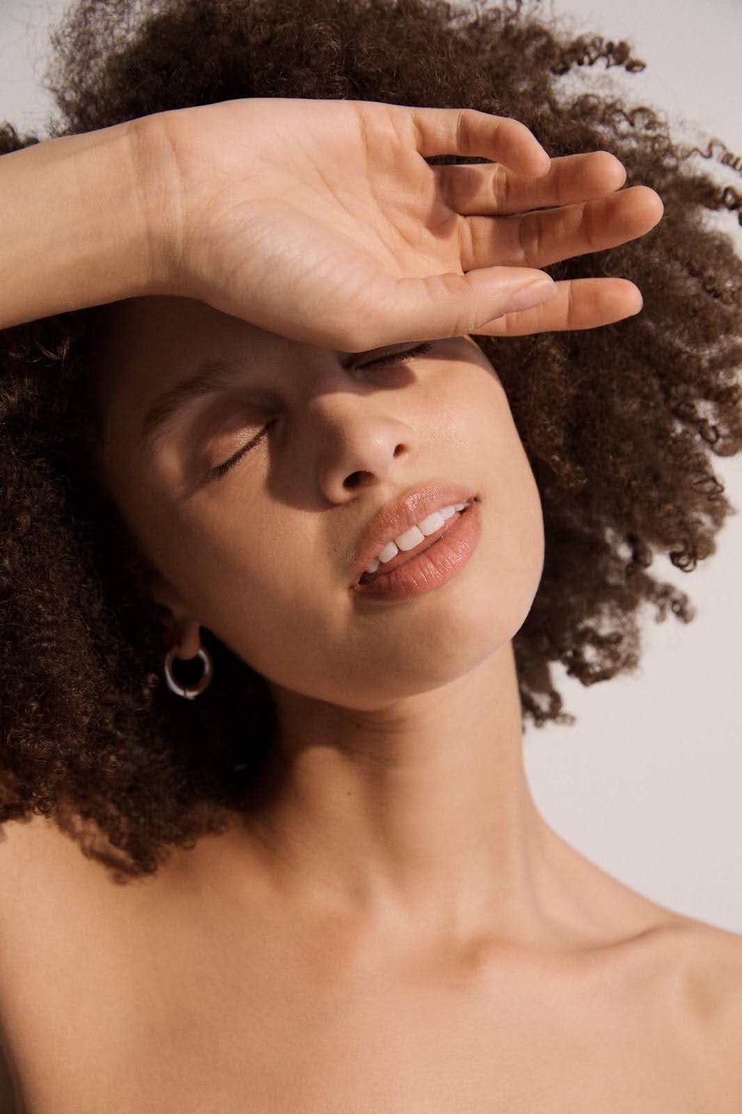 Young woman with radiant skin, eyes closed and hand resting on forehead