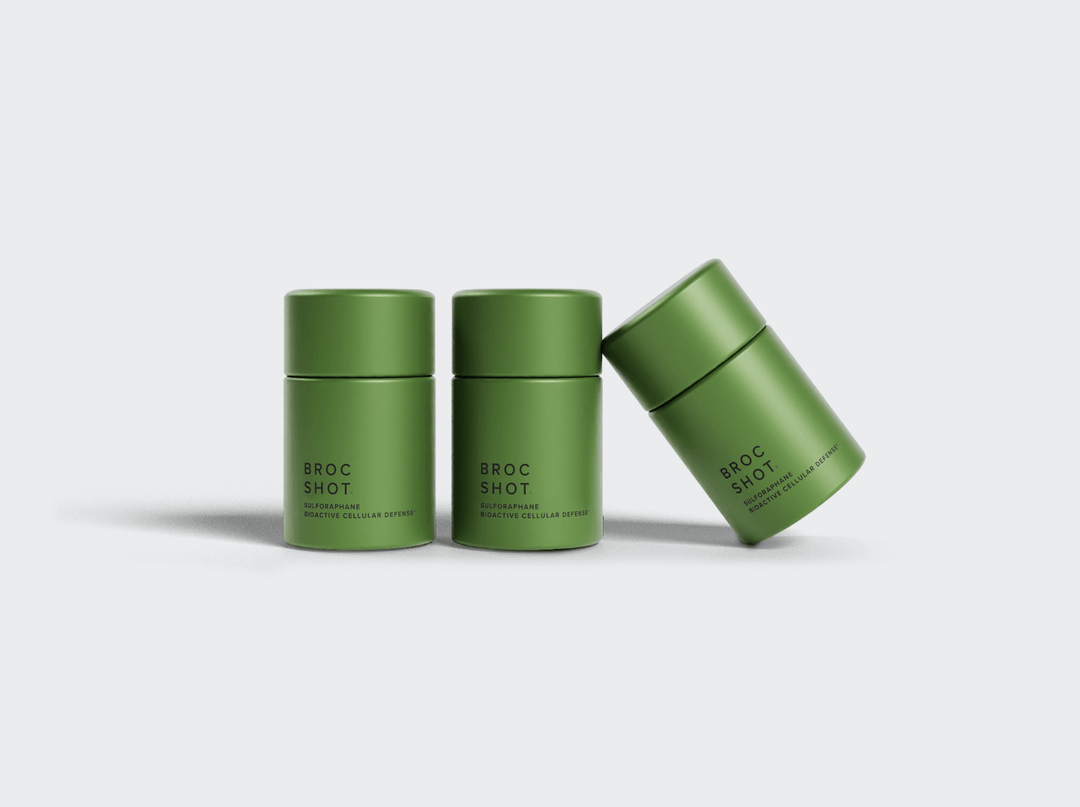 Three green supplement jars, one tilted, labeled "BROC SHOT" and "SULFORAPHANE BIOACTIVE CELLULAR DEFENSE". 