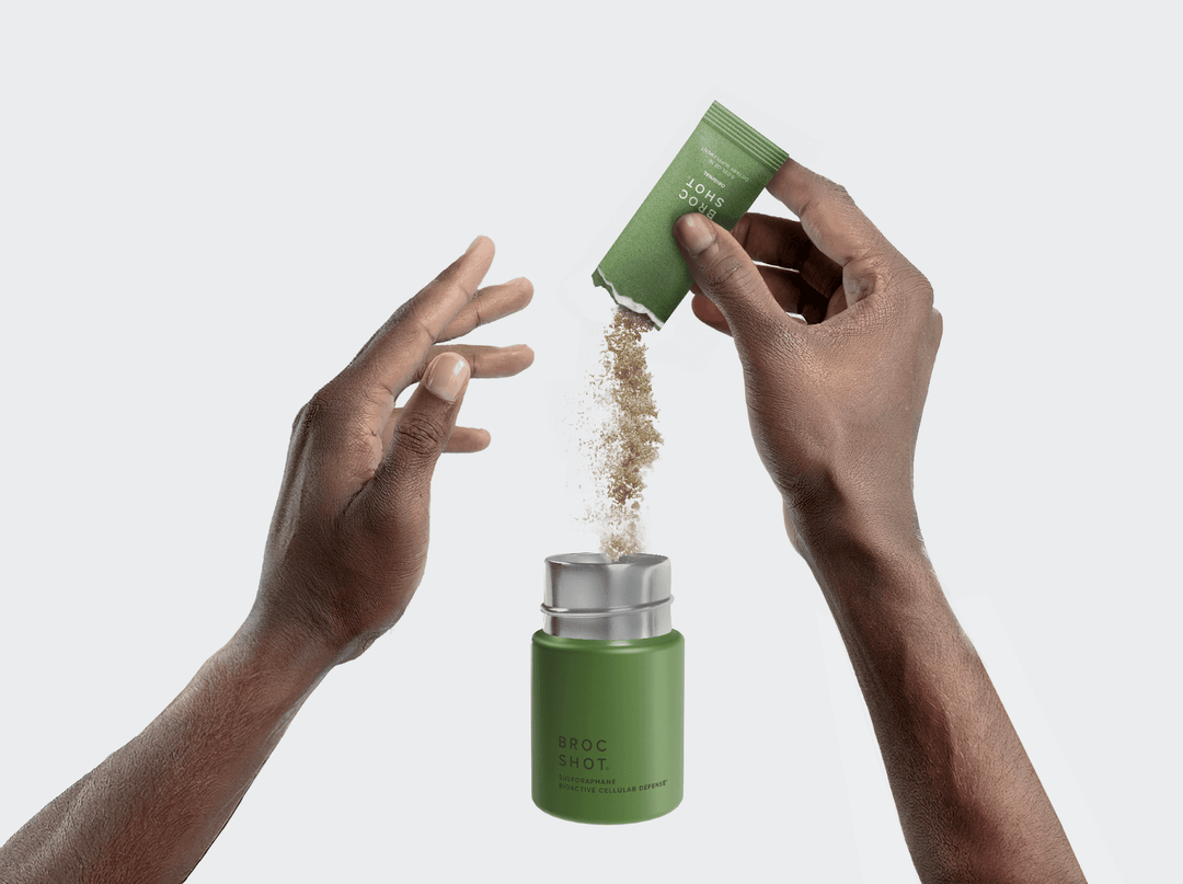 Two hands pouring powder from a green packet labeled 'BROC SHOT' into a green supplement jar labeled 'BROC SHOT'. 