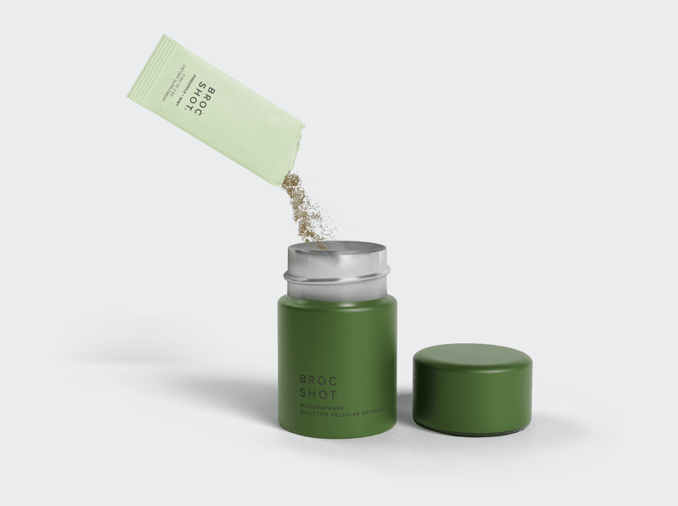 Angled view of Broc Shot sulforaphane powder sachet pouring into open green jar with a pale gray background