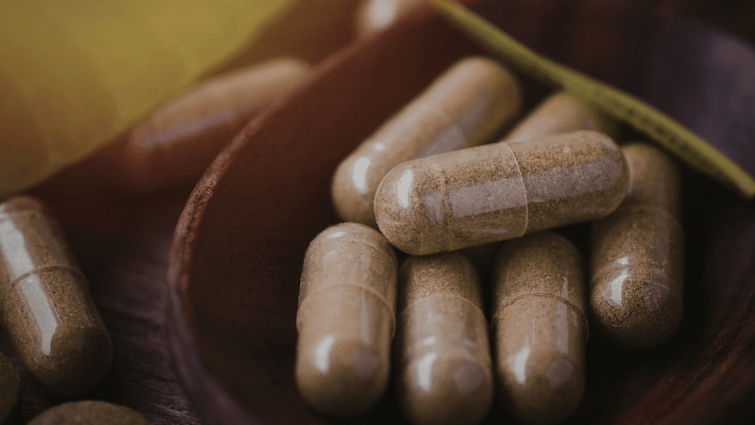 Close up of sulforaphane supplement capsules showing powder-filled clear capsules resting in a wooden spoon on a dark surface