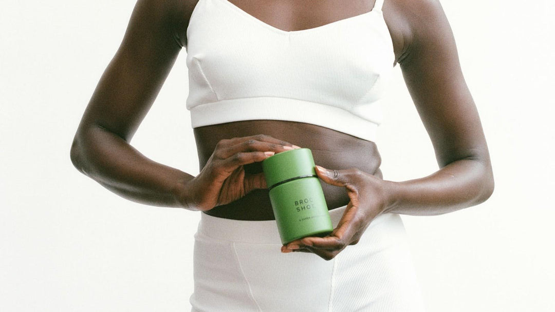 Front view of Broc Shot jar showcasing matte green packaging held at a woman's midsection on a white background
