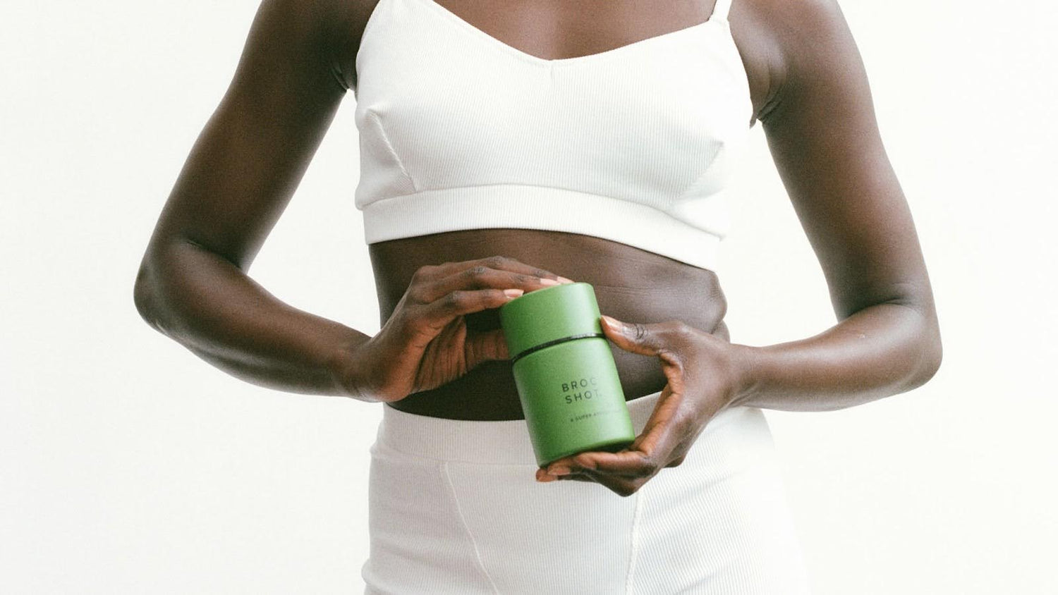 Front view of Broc Shot jar showcasing matte green packaging held at a woman's midsection on a white background