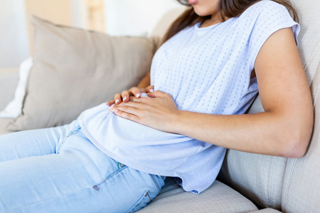 Woman reclining on a couch holding her lower abdomen and appearing to have stomach discomfort