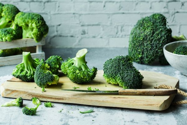 Broccoli florets on a wooden cutting board with a knife and a rustic brick-wall background