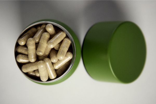 Top view of Broc Shot sulforaphane supplement capsules in an open green container beside its lid on a white background