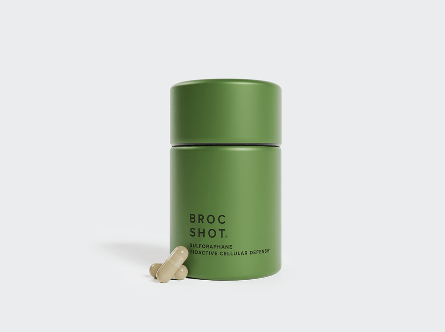 Front view of green stainless steel Broc Shot capsule jar with branded label and two beige capsules on light gray background