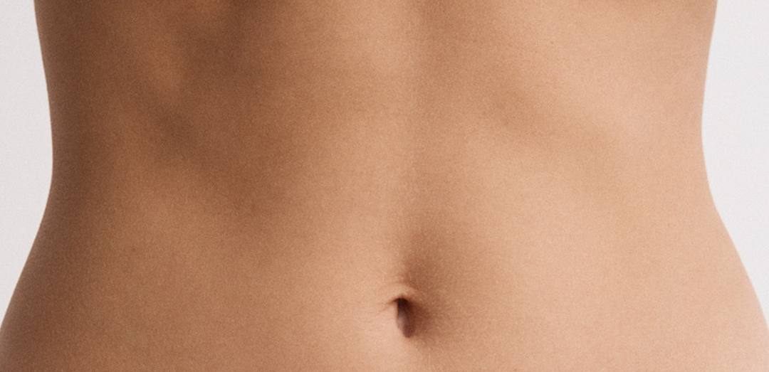 Close-up of a bare midsection showing a flat stomach and navel against a plain light background