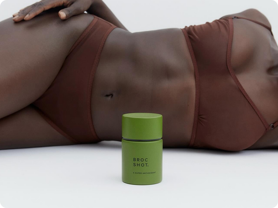 Front view of Broc Shot green jar showcasing matte packaging and label with a reclining model in brown underwear behind